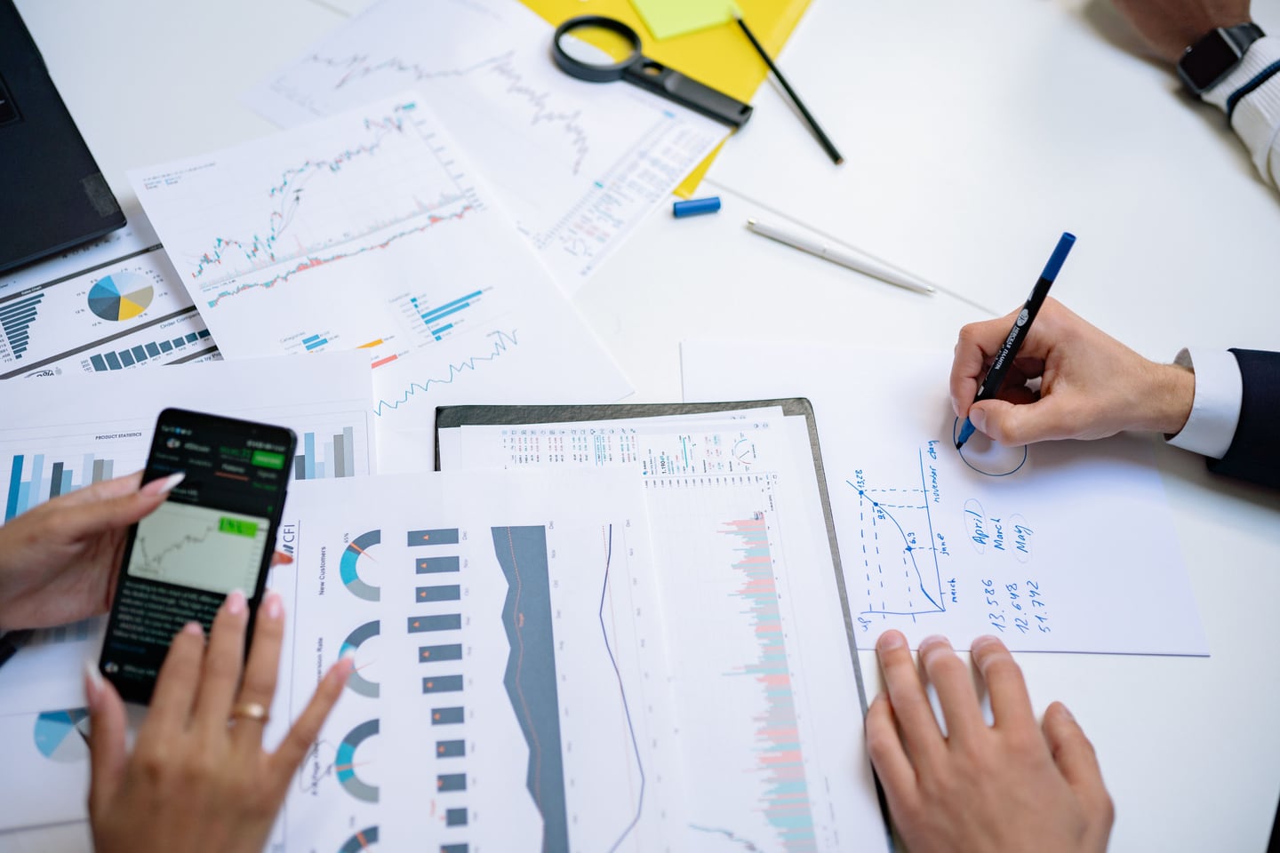 Hands hold a phone and write notes beside printed charts.