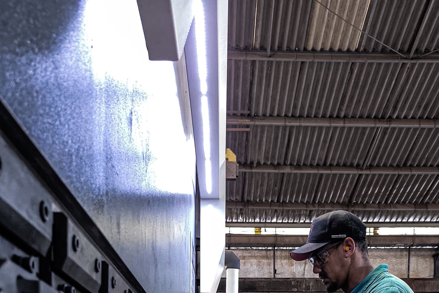 A factory worker measures sheet metal at an industrial machine.
