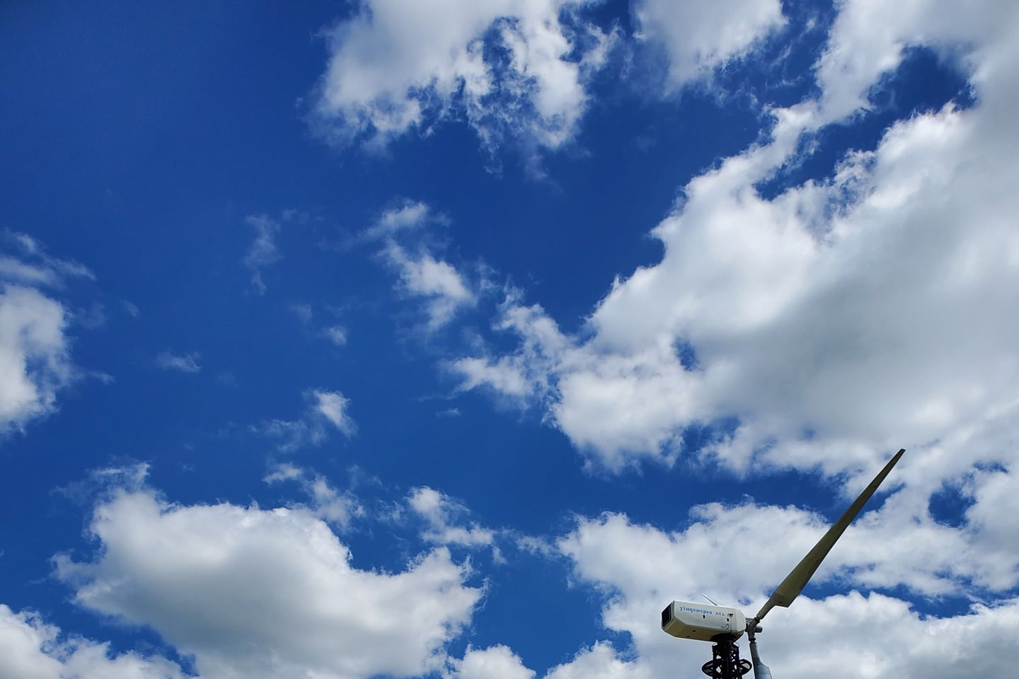 Wind turbines stand beneath a wide, clouded sky.